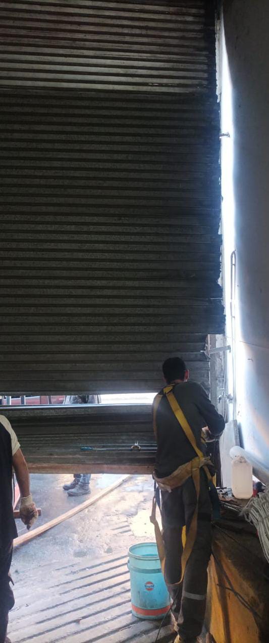 Técnico reparando cortina metálica en comercio con herramientas profesionales